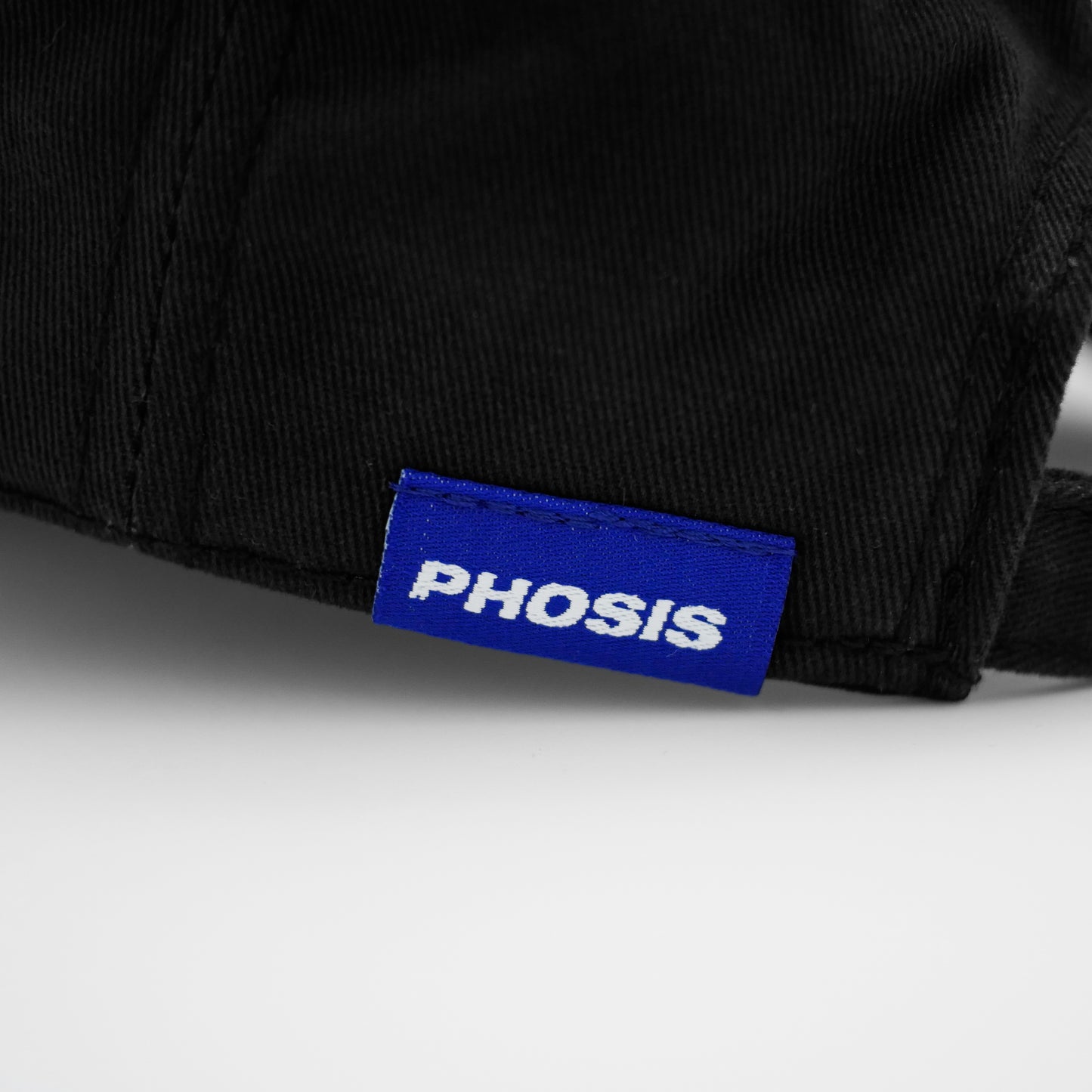 Close up view of the woven label in the BRUISED black dad hat from PHOSIS® Clothing